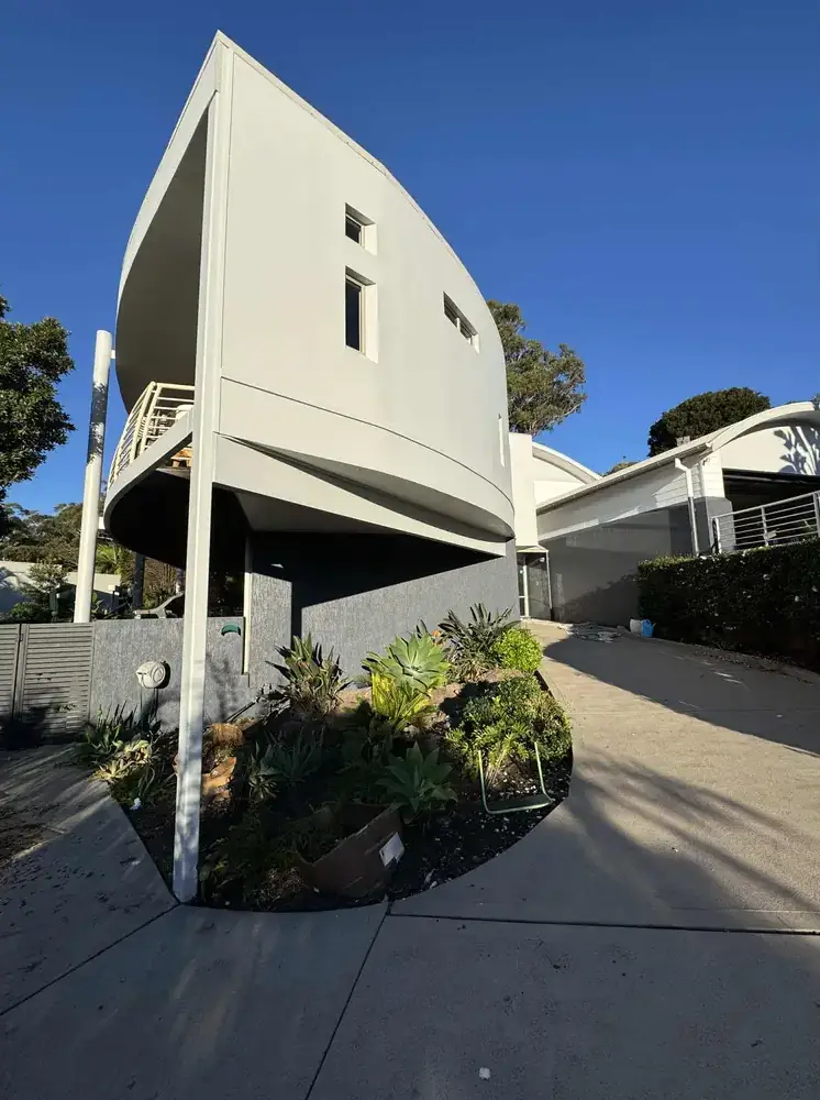 Cream-painted elevated modern home above a curved driveway