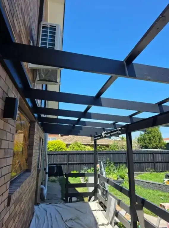 Repainted pergola with dark beams against timber cladding
